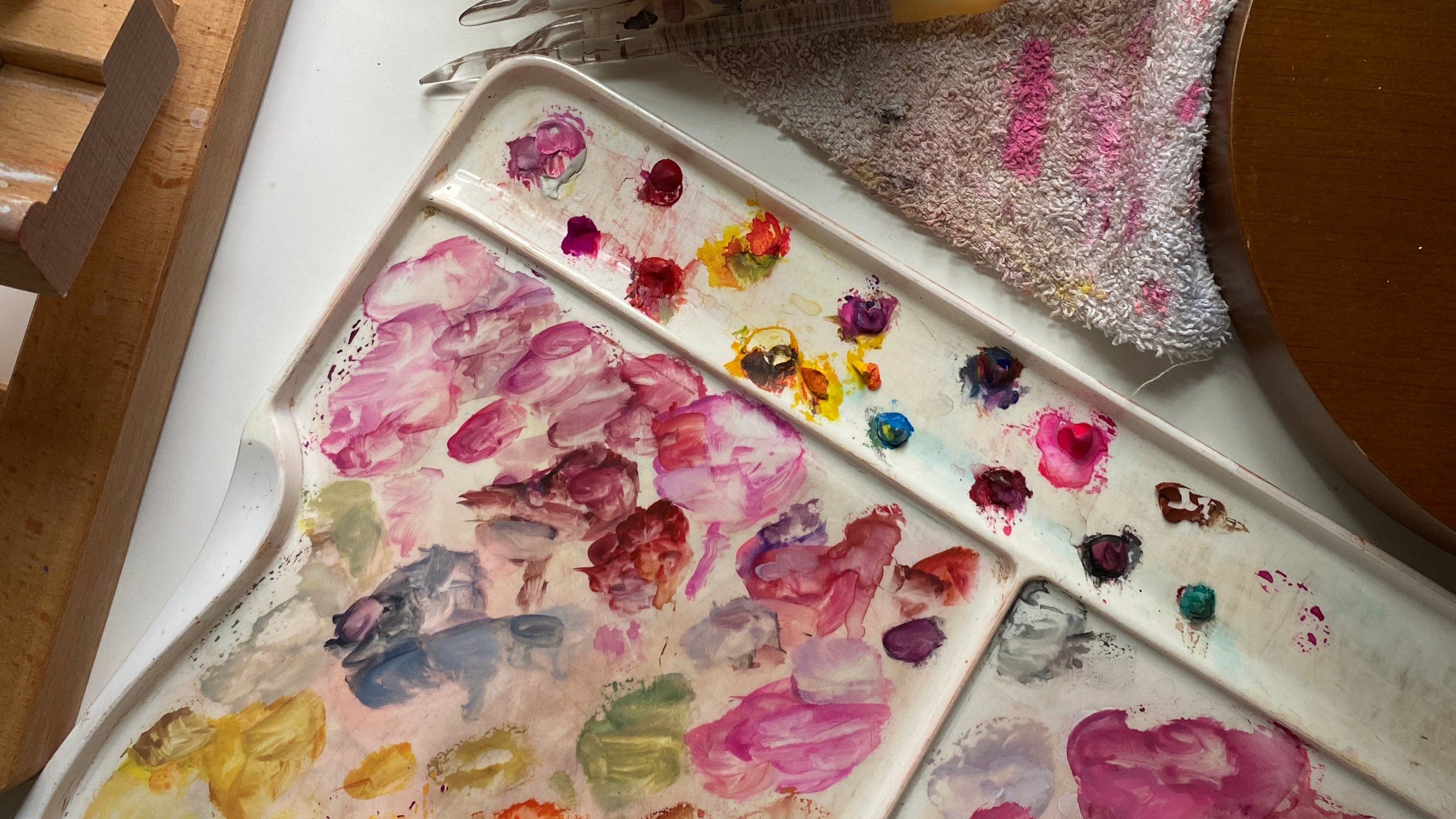 Art supplies including a palette with paint, a cup of tea, and art materials on a table.